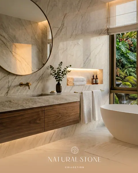 Pale veined stone is used for the bathroom walls and floor, alongside timber cabinetry and a round mirror.