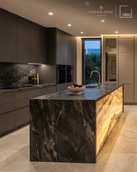 Dark stone with light veining is used for the kitchen island and work surfaces, alongside a golden glow and contrasting dark finishes.