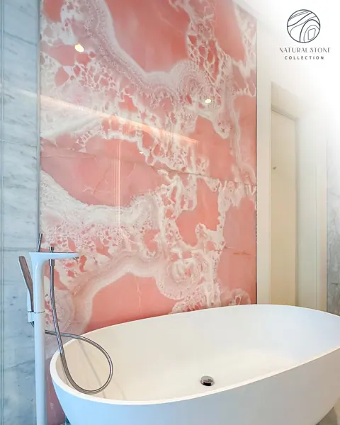 Rose coloured veined stone is used for the bathroom walls and floor, alongside a freestanding white bath and soft lighting.
