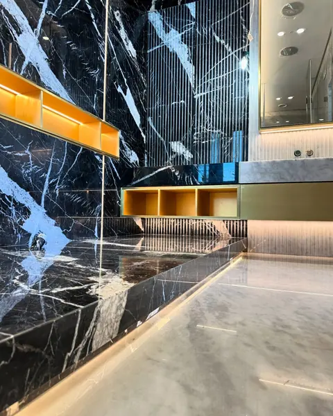 Black marble with white veining is used for the bathroom walls and floor, alongside warm metallic details and carefully placed lighting.