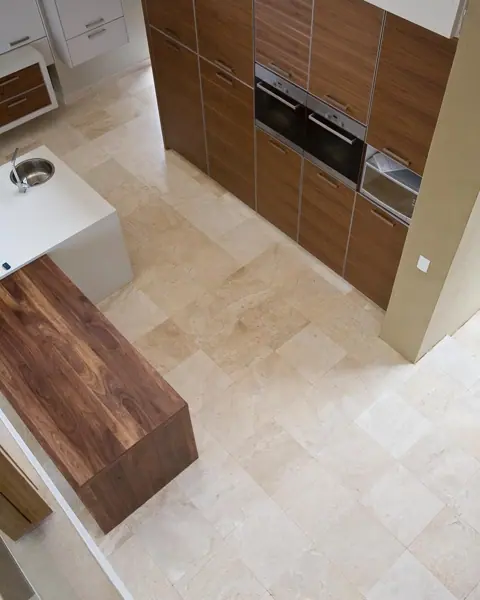 Soft cream stone is used for the floor throughout the room, alongside light cabinetry and warm timber finishes.