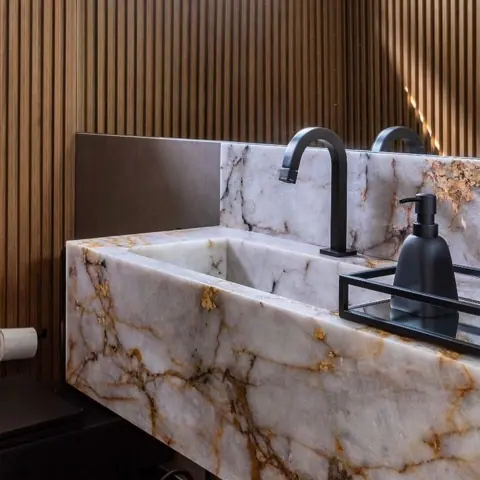 White stone with golden veining is used for the vanity and its surrounding surfaces, alongside vertical timber detailing and warm concealed lighting.