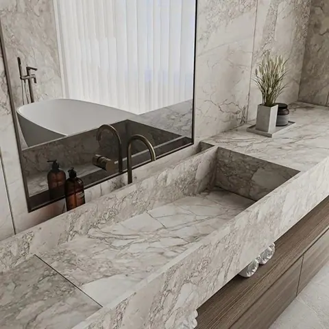 Pale veined stone is used for the vanity and its surrounding surfaces, alongside large mirrors and a clean vanity composition.