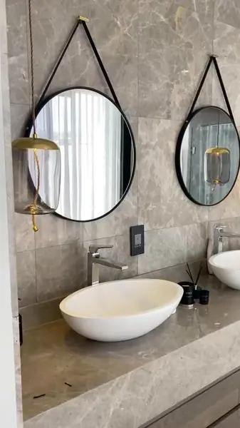 Grey veined stone is used for the vanity and its surrounding surfaces, alongside timber cabinetry and a round mirror.