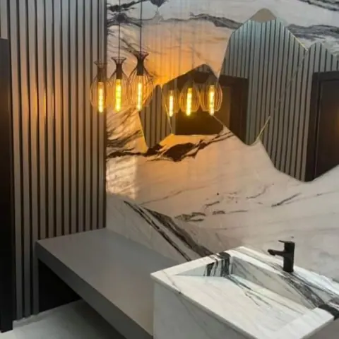 Pale veined stone is used for the vanity and its surrounding surfaces, alongside vertical timber detailing and warm concealed lighting.