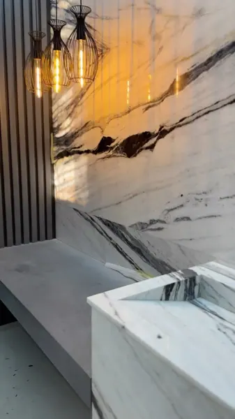 White marble with grey veining is used for the vanity and its surrounding surfaces, alongside a golden glow and contrasting dark finishes.