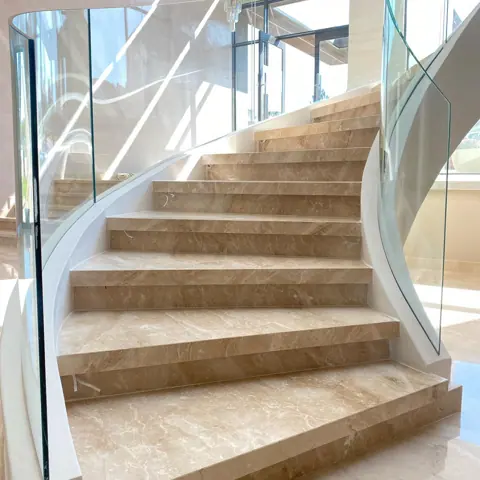 Warm beige natural stone is used for the stair treads and landings, alongside glass balustrades and generous daylight.