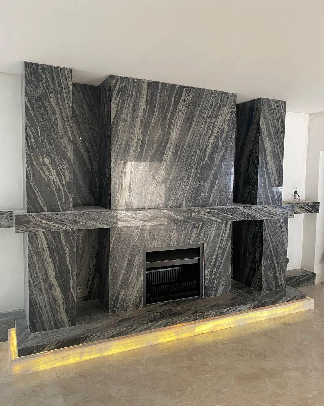 Stone with mirrored veining is used for the fireplace surround, alongside a golden glow and contrasting dark finishes.