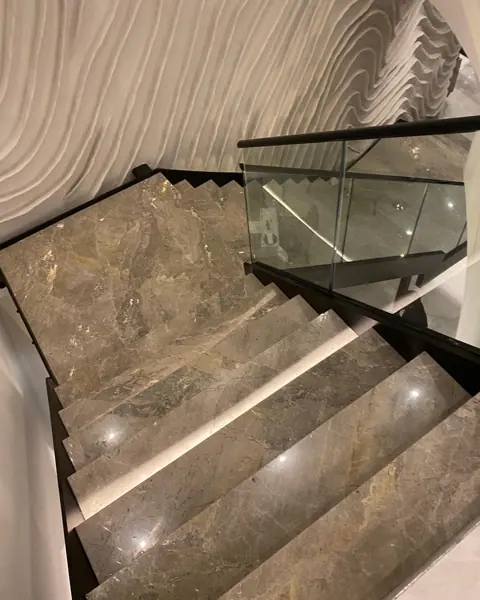 Rich brown veined stone is used for the stair treads and landings, alongside glass balustrades and generous daylight.