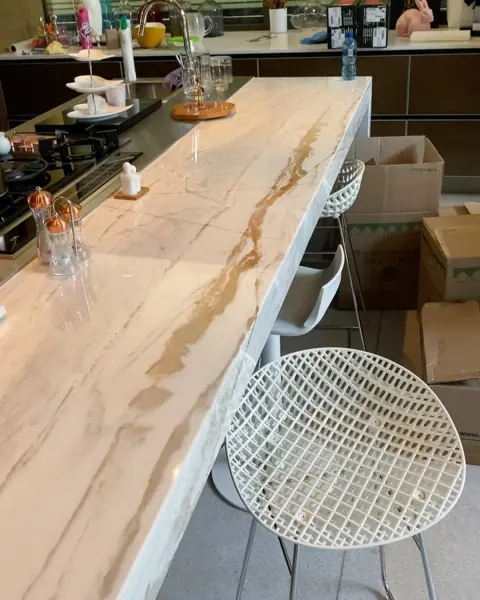 White stone with golden veining is used for the breakfast counter, alongside white dining chairs and a light interior palette.