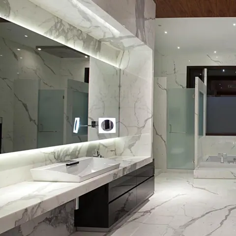 White marble with grey veining is used for the bathroom walls and floor, alongside large mirrors and a clean vanity composition.