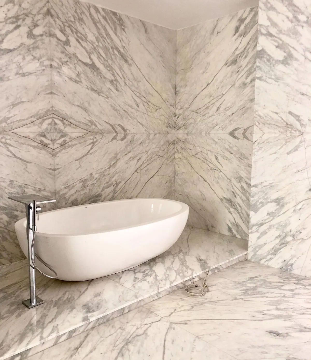 Stone with mirrored veining is used for the bathroom walls and floor, alongside a freestanding white bath and soft lighting.