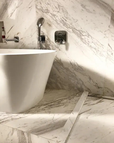 White stone with golden veining is used for the bathroom walls and floor, alongside a freestanding white bath and soft lighting.