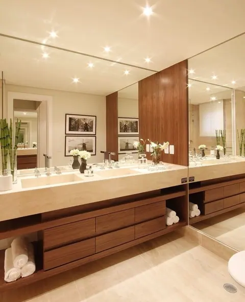 Soft cream stone is used for the vanity and its surrounding surfaces, alongside light cabinetry and warm timber finishes.