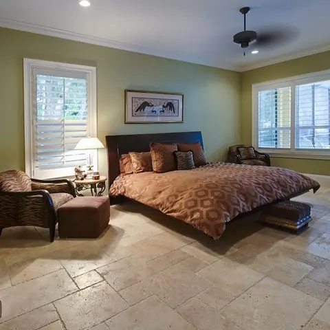 Warm beige natural stone is used for the floor throughout the room, alongside tall windows and a bright neutral interior.