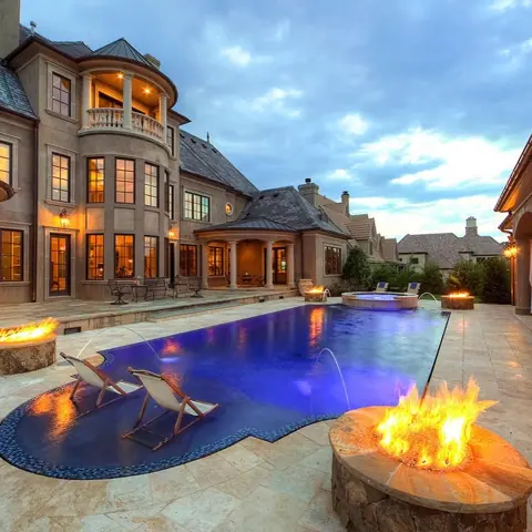 Warm beige natural stone is used for the poolside terrace, alongside a linear fireplace and warm accent lighting.