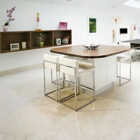 Soft cream stone is used for the kitchen floor and surrounding surfaces, alongside light cabinetry and warm timber finishes.