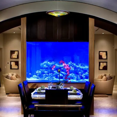 Warm beige natural stone is used for the floor throughout the room, alongside a large illuminated aquarium and dining furniture.