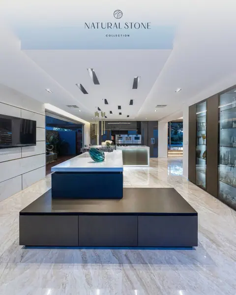 Expansive stone flooring sets a bright foundation beneath bold kitchen islands, dark wall cabinetry and a long, streamlined ceiling.