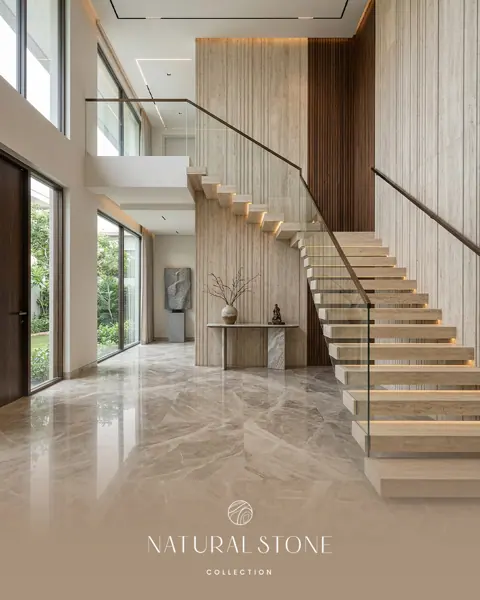 A slender staircase rises beside tall windows, above a flowing stone floor that links the entrance to the sculpted wall behind it.
