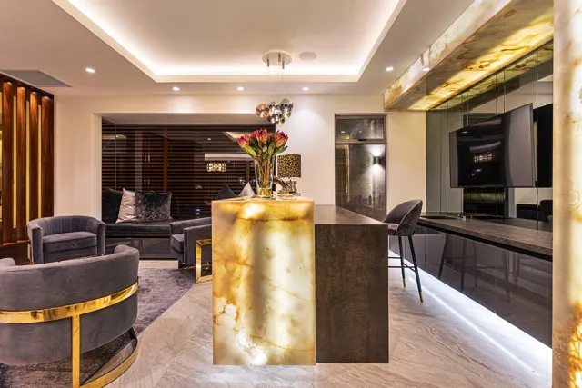 A glowing golden stone island anchors this kitchen, with dark cabinetry and a softly lit ceiling completing the layered interior.