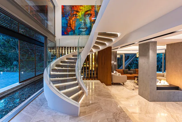 A sweeping staircase, veined floor and warm timber panels create a generous entrance, linking the stone surfaces to the living area.
