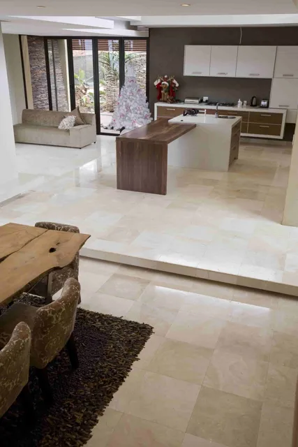 Pale stone tiles flow from the foreground into the kitchen and living area, creating a continuous visual connection between the spaces.