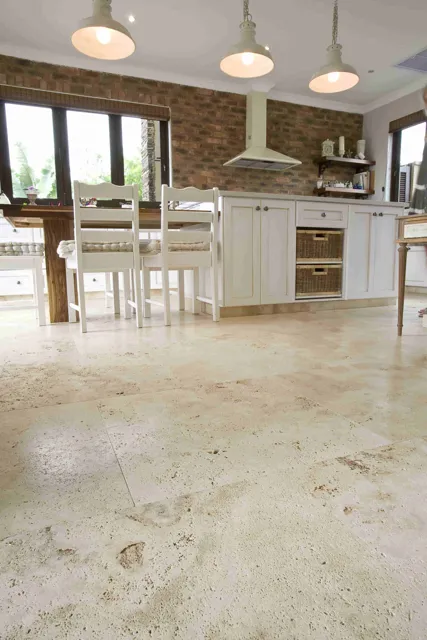 Natural colour variation in the floor complements a light kitchen island, timber cabinetry and pendant lighting in this open interior.