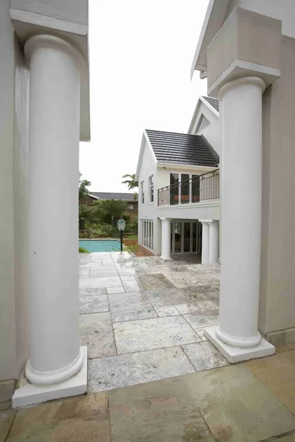 Cream paving stretches between white columns toward the courtyard, combining natural stone texture with traditional architectural proportions.