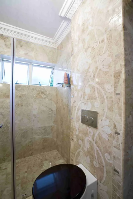 Stone wall tiles extend into a glass shower enclosure, with pale mineral patterns and a high window bringing texture and light to the bathroom.